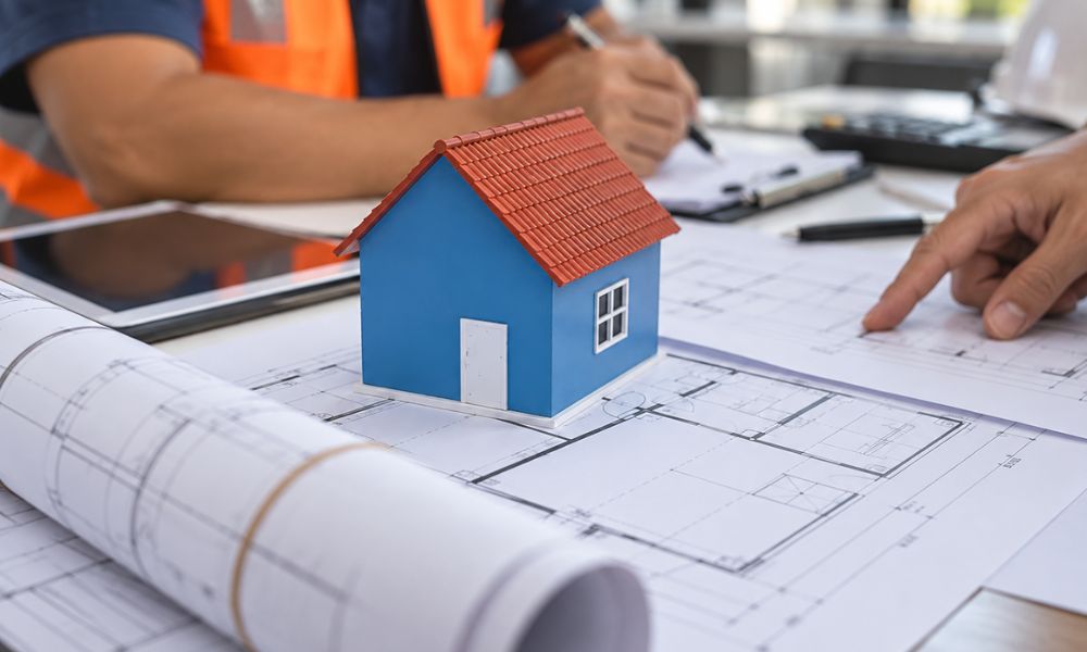 Miniature house model on architectural blueprints as professionals review roofing documents and property plans.
