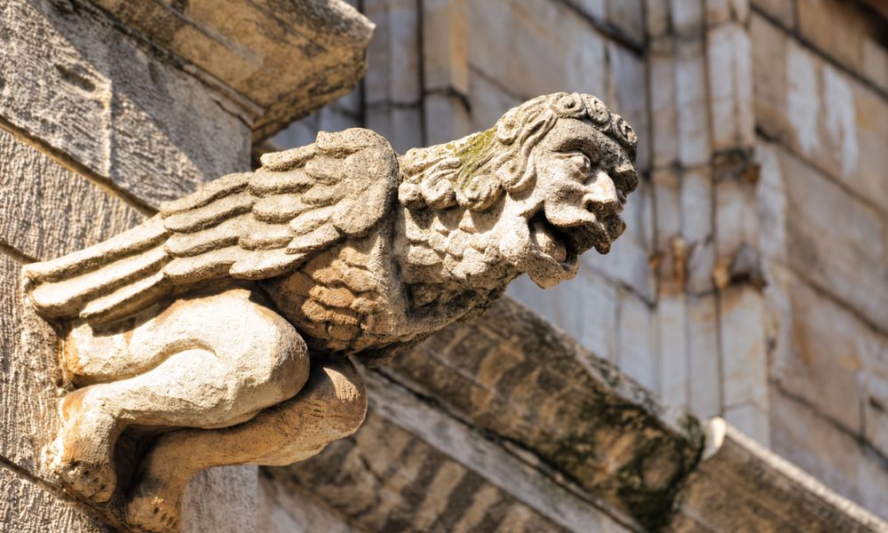 Winged stone creature with a human face projecting from a masonry wall