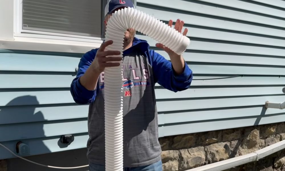 Man holding a flexible white vinyl downspout extension outside a house.